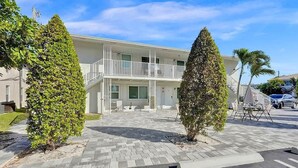 A two-story building with a balcony, paved walkway, and two conical trees. - Bright Studio | Walk to Pompano Beach & Pier (Pompano Beach)