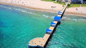 A pier extending into a turquoise sea with a beach in the background.