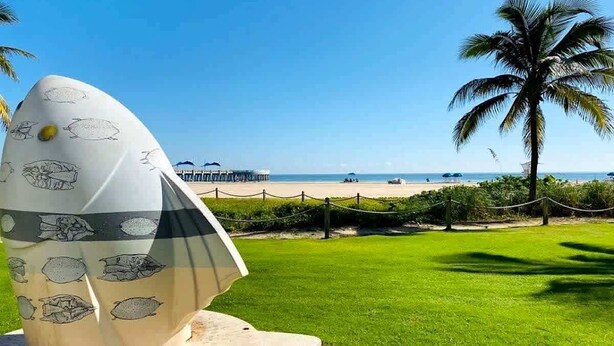 A sculpture of an egg with fish patterns, a palm tree, and a beach in the background. - Bright Studio | Walk to Pompano Beach & Pier (Pompano Beach)