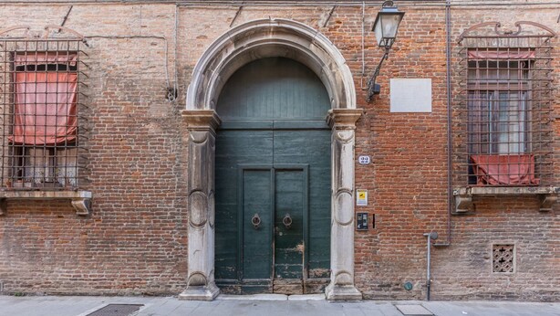 Un edificio de ladrillo con una puerta verde, dos ventanas con rejas de metal y una farola.