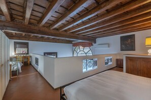 A bedroom with a wooden ceiling, a bed, a desk, and a window with decorative iron bars.