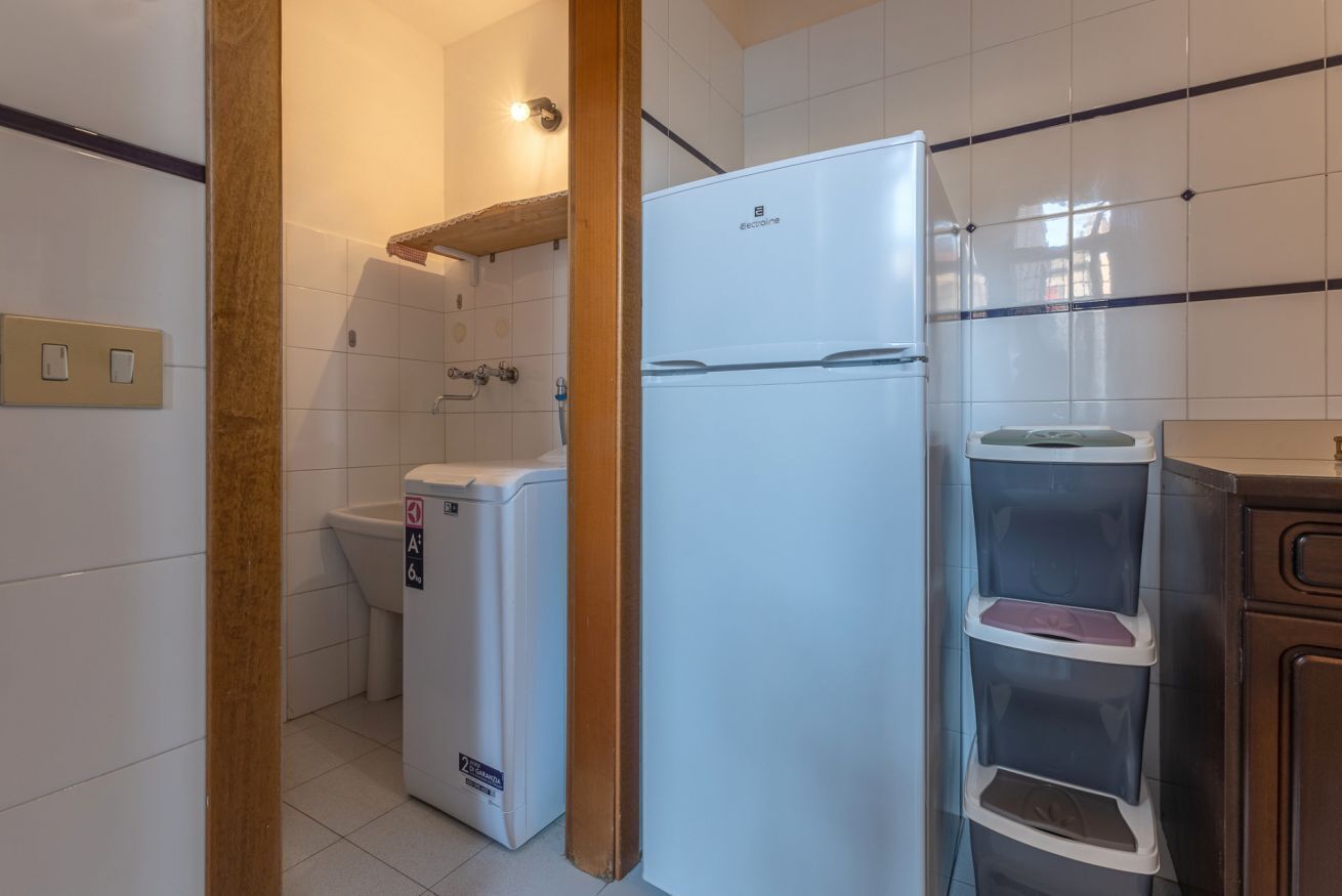 Une cuisine compacte équipée d’un réfrigérateur encastré, d’un lave-linge et d’un petit meuble avec des étagères.