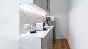 Une cuisine moderne avec un plan de travail blanc, un four encastré et une bouilloire en acier inoxydable.