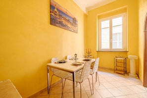 A dining area with a table set for four, a window with shutters, and a painting on the wall.