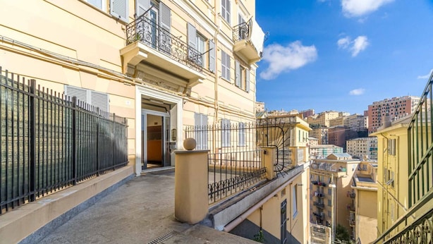 A multi-story building with balconies, a central entrance, and a view of the cityscape.