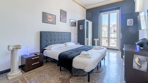 A hotel room with a bed, a nightstand, a desk, and a large window with a city view.