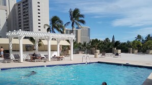 A swimming pool with lounge chairs and a pergola, surrounded by palm trees and buildings. - Cozy studio condo in wonderful Honolulu with WiFi, fitness room (Honolulu)