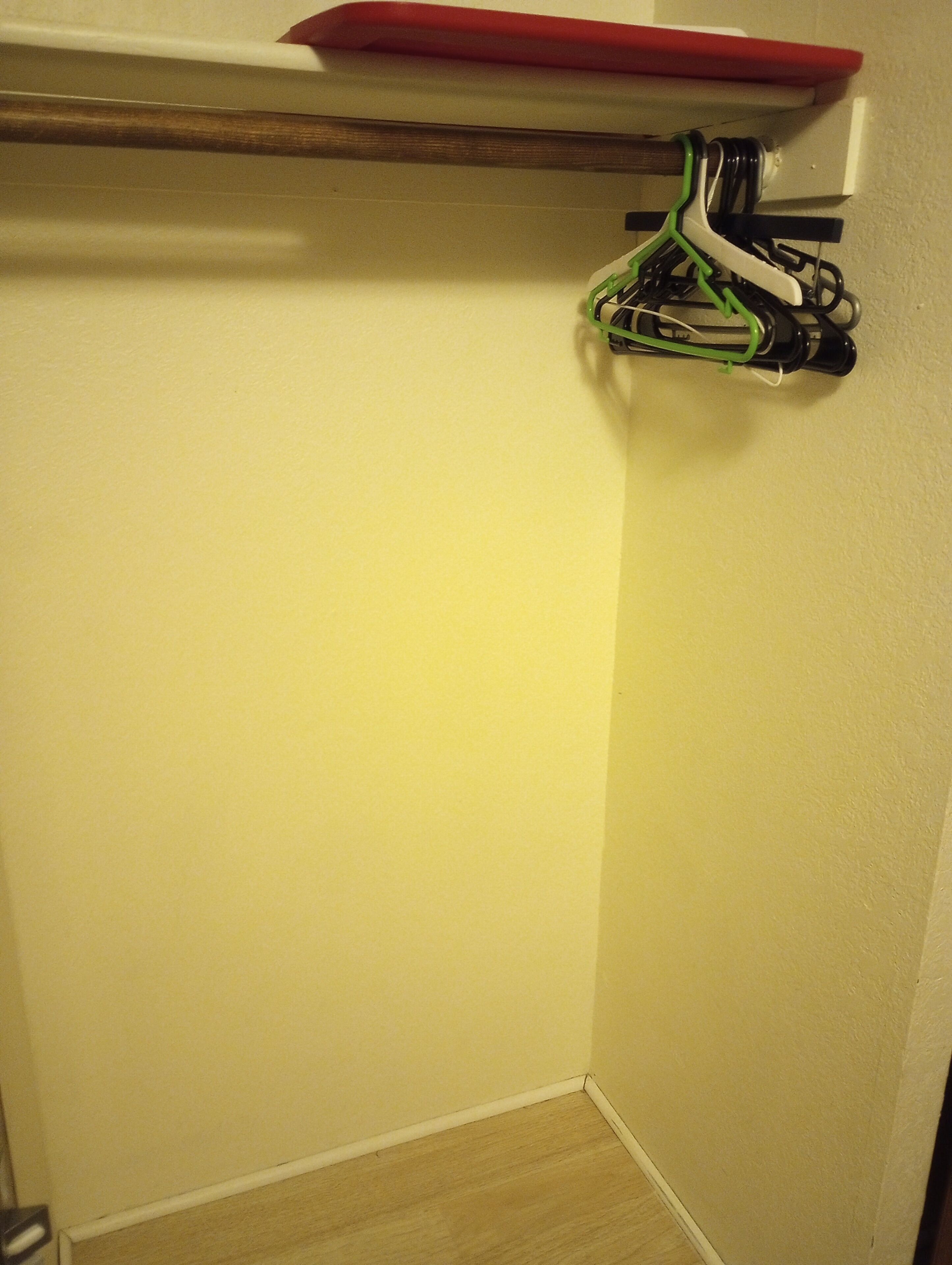 Un rincón de una habitación con suelo de madera, pared blanca y un objeto rojo en una estantería.