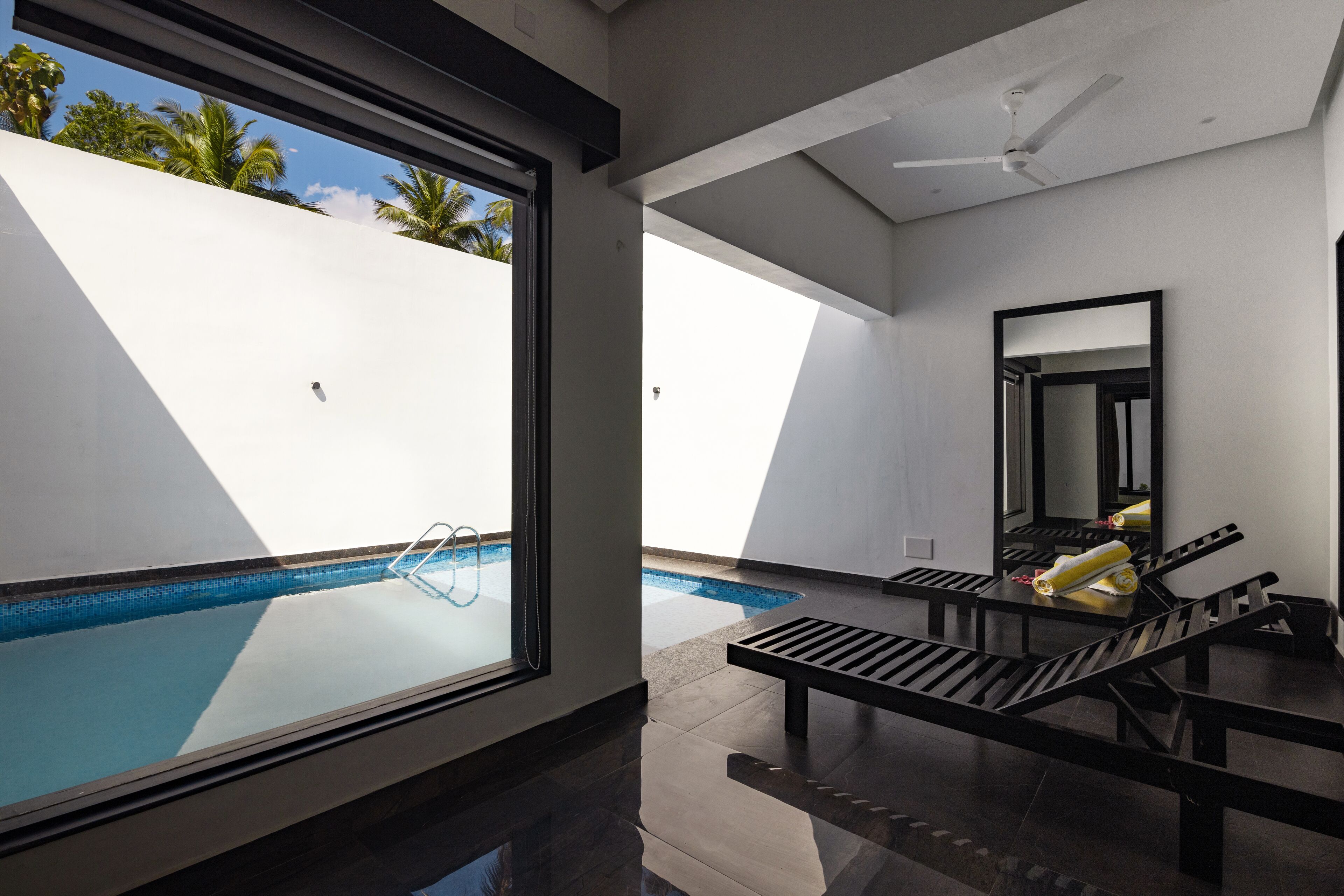 A modern room with a glass wall, a pool, and a ceiling fan.