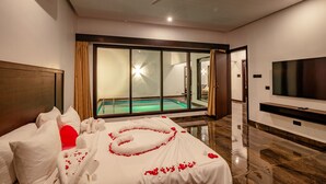 A hotel room with a bed, a TV, a ceiling fan, and a view of a swimming pool. - The Saravi Resort (Vanur)