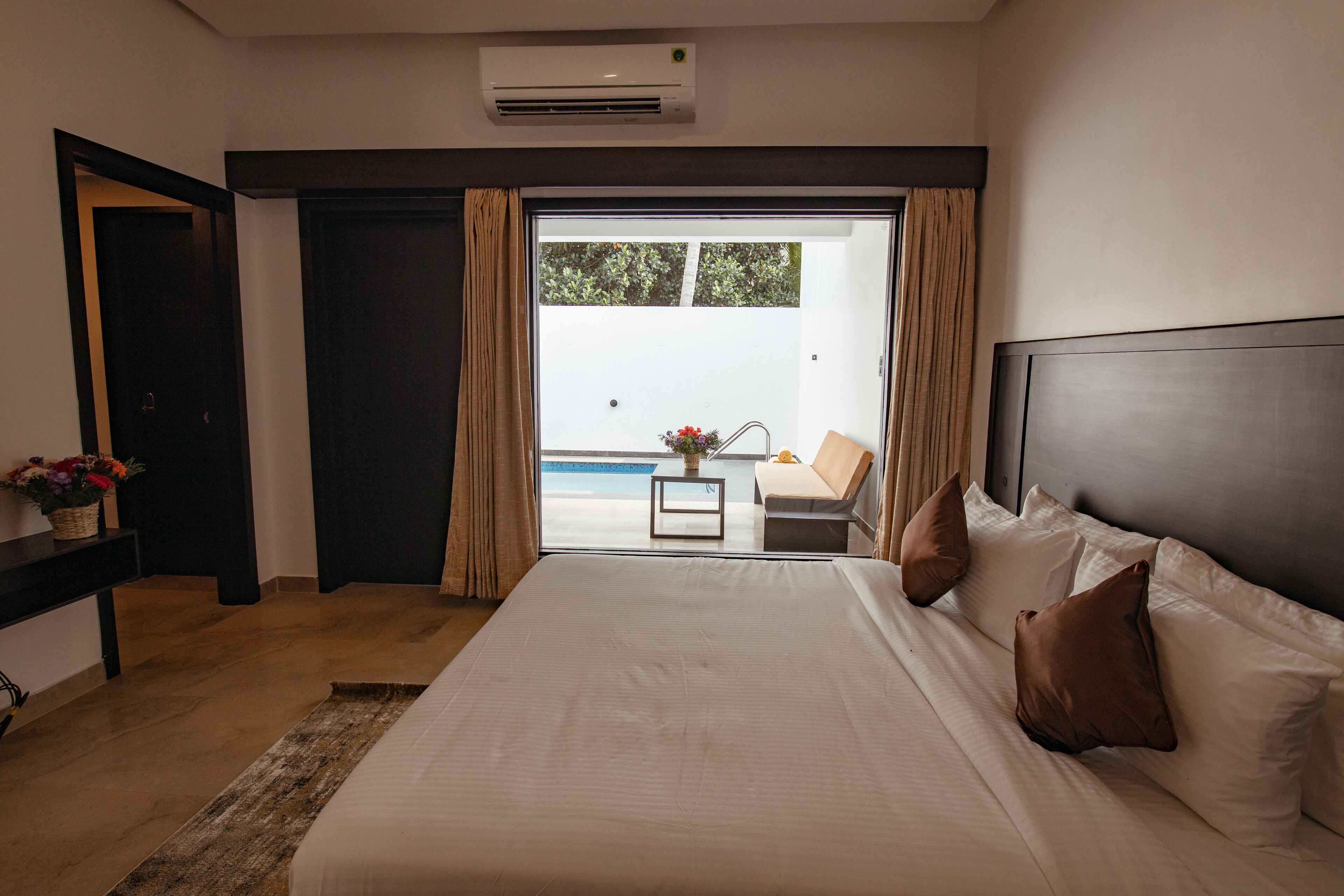 A hotel room with a large bed, a small table, and a view of a pool and outdoor seating.