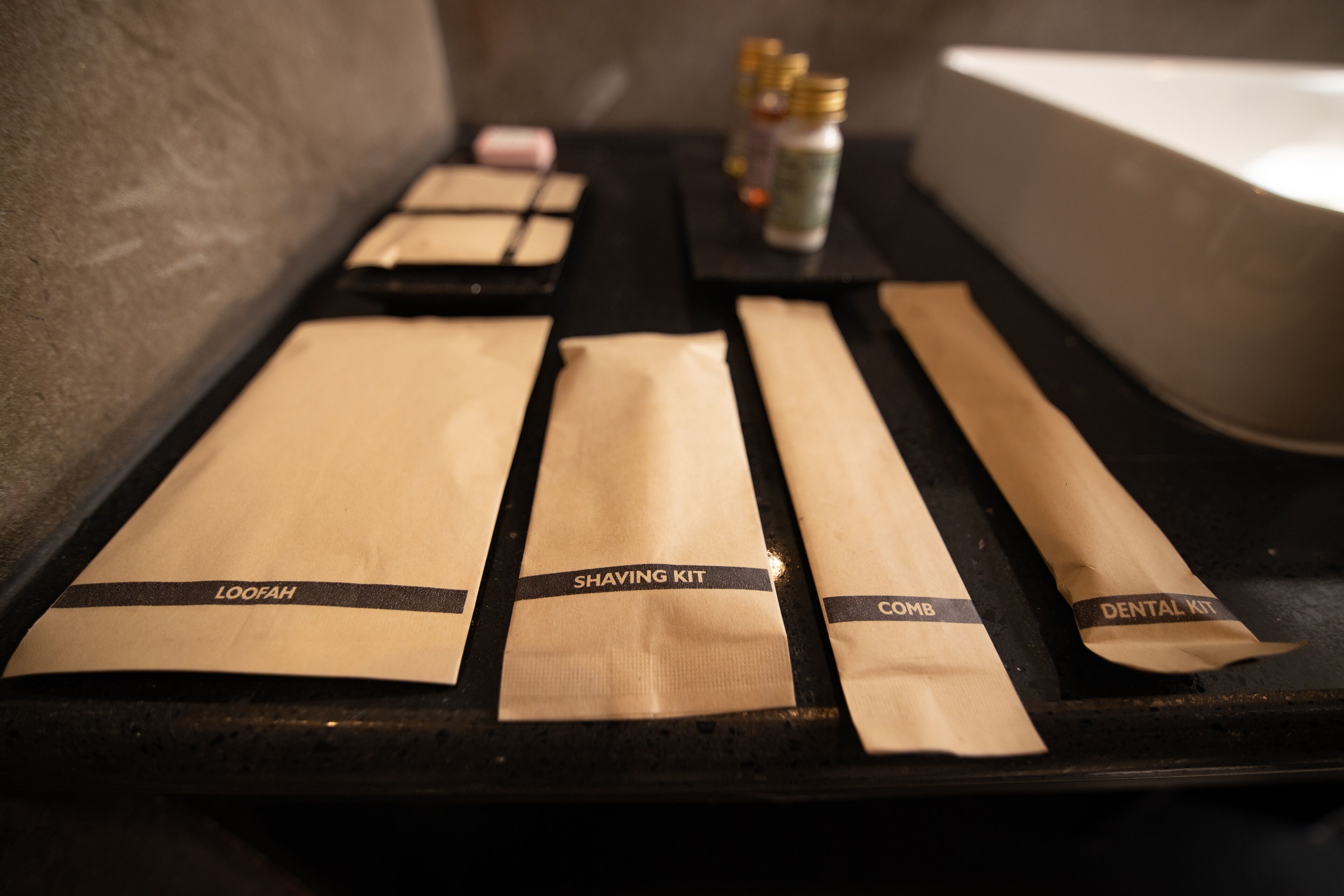 Una bandeja con varios paquetes etiquetados como 'LOOFAH', 'KIT DE AFEITADO', 'PEINE' y 'KIT DENTAL'.