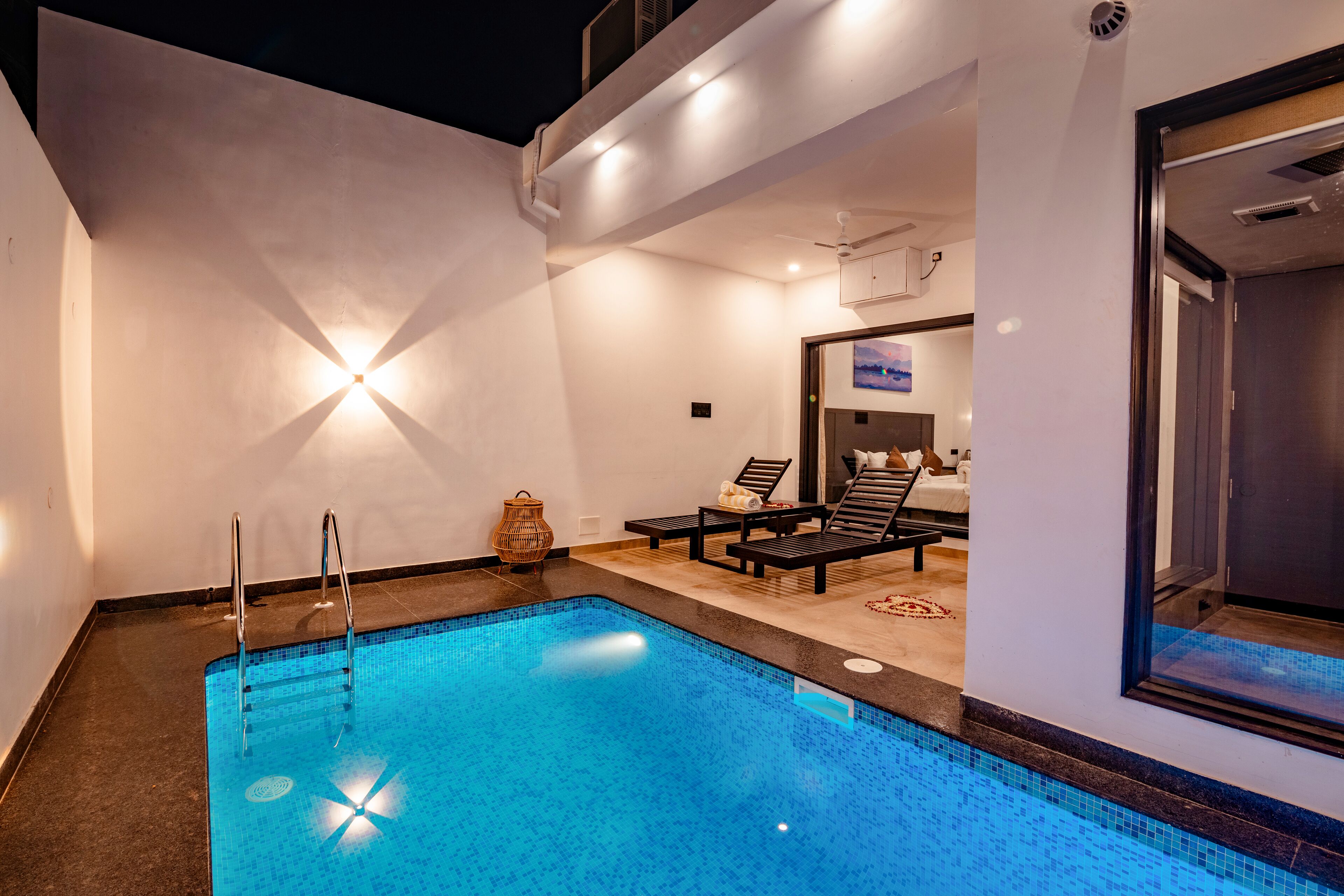 A swimming pool with a tiled edge, a lounge area with a sofa and chairs, and a ceiling fan.