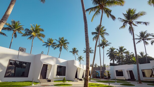 A modern building with large windows and a paved courtyard surrounded by palm trees. - The Saravi Resort (Vanur)