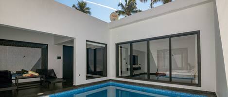 A modern pool area with a clear blue pool, large sliding glass doors, and a white exterior wall.