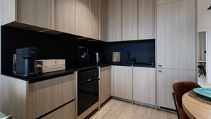 A modern kitchen with wooden cabinets, a black countertop, a coffee machine, and a small dining area with a table and chair. - Cuero | Centrum | Garaż podziemny | Dwie sypialnie (Bydgoszcz)