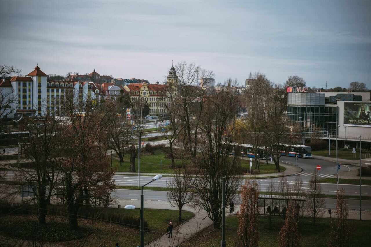 Bybillede med historiske bygninger, en rundkørsel og en moderne busstation.