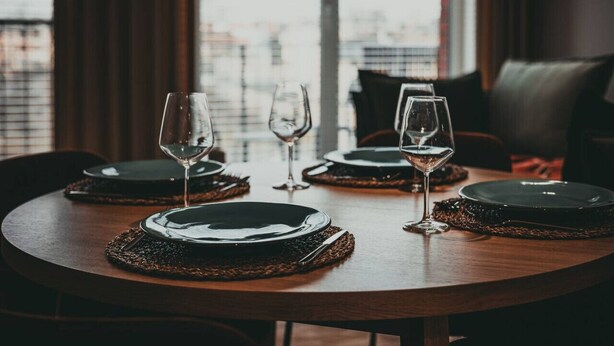 A dining table set with plates, cutlery, and wine glasses, with a view of buildings through a window. - Cuero | Centrum | Garaż podziemny | Dwie sypialnie (Bydgoszcz)