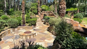 Un chemin de pierres qui traverse un jardin, avec un espace de repos circulaire et une petite cascade.