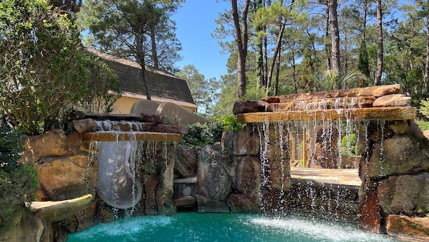 Une piscine naturelle avec une cascade, entourée de rochers et d’arbres.