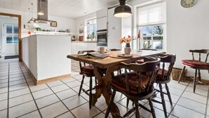 Une cuisine moderne avec des meubles blancs, un îlot central et un coin repas comprenant des chaises et une table en bois.