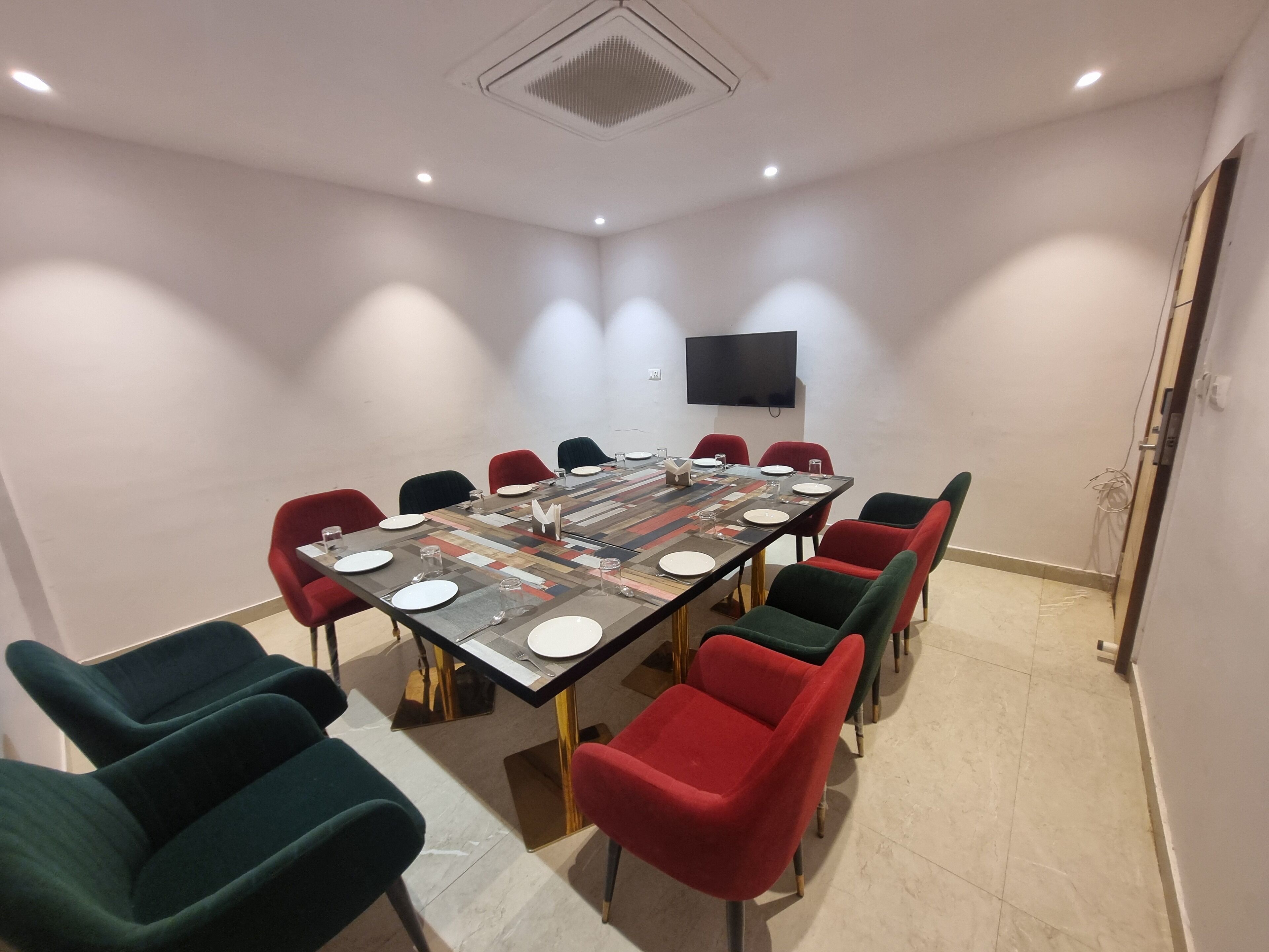 Un salón de conferencias con una mesa rectangular, varias sillas y un televisor de pantalla plana en la pared.