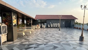 A rooftop terrace with a geometric tile floor, outdoor seating, and a building with a red-tiled roof.