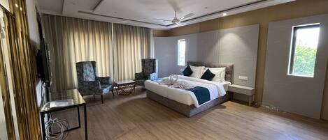 Habitación de hotel moderna con una cama grande, dos sillones, una mesita, un televisor y una ventana con cortinas.