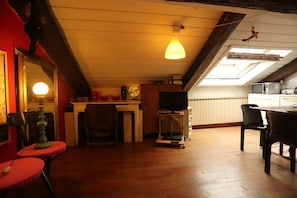 Una sala de estar acogedora con techo de madera, una mesa de comedor, un televisor y una zona de cocina con microondas.