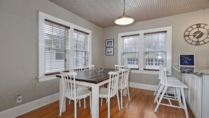 A dining area with a wooden table and white chairs, large windows with blinds, a wall clock, and a welcome sign. - 2 Living Areas & Kids' BunkRoom (Springfield)