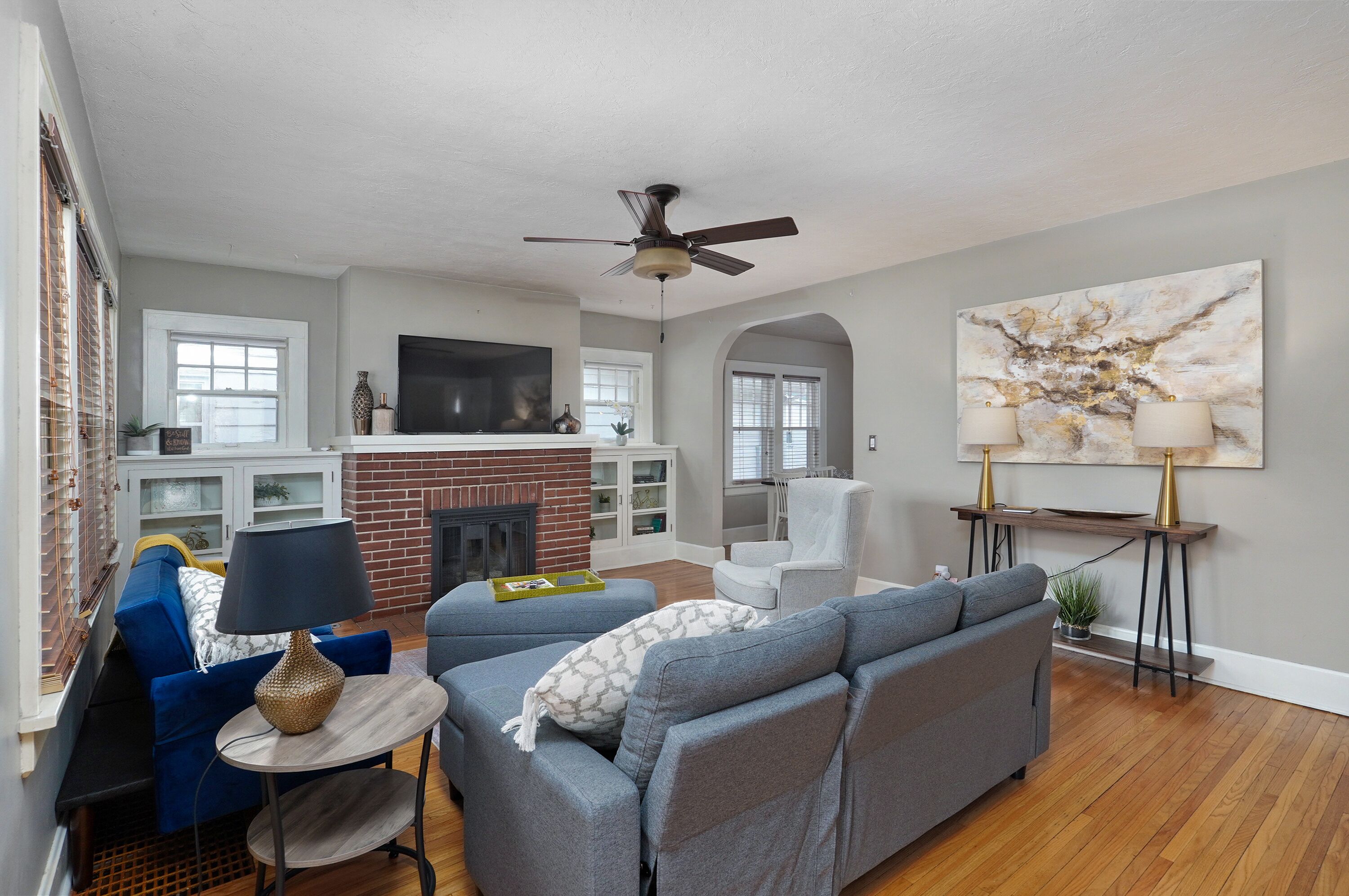 A living room with a fireplace, a ceiling fan, a TV, and a large abstract painting.