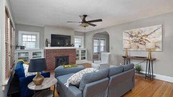 A living room with a fireplace, a ceiling fan, a TV, and a large abstract painting.