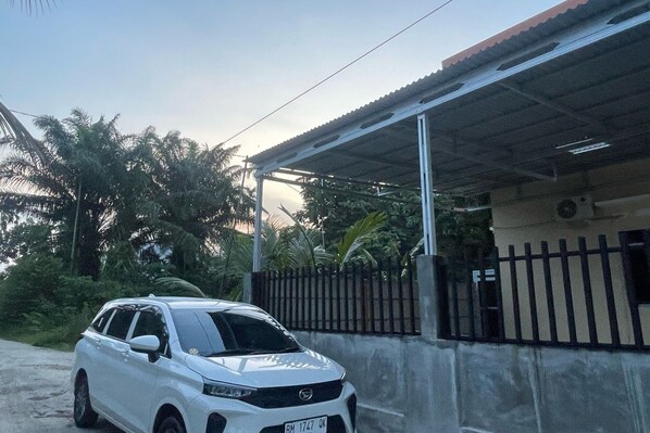 Une voiture blanche est garée devant un bâtiment dont le toit est en métal et qui est entouré d’une clôture noire.