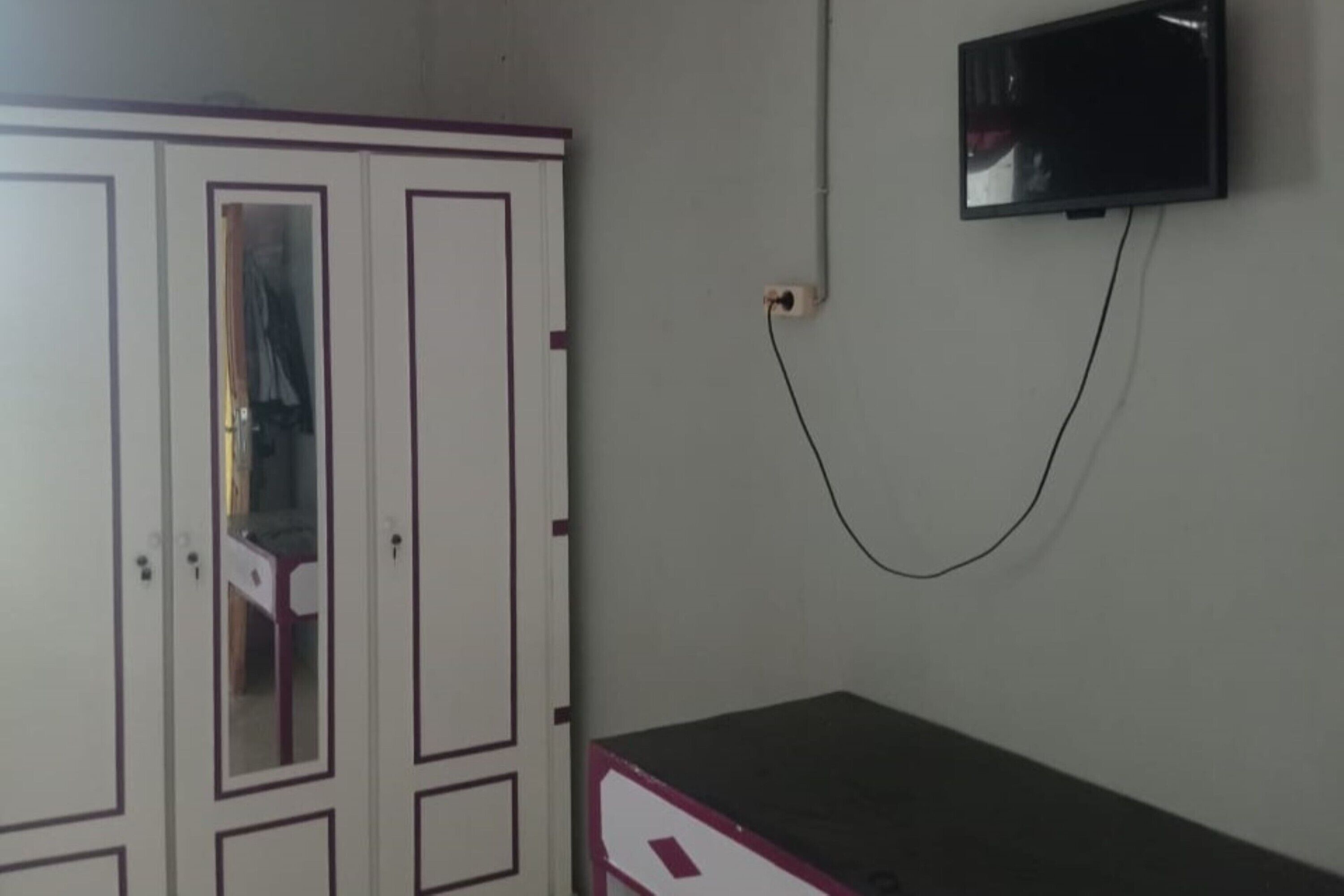 A room with a wardrobe, a television mounted on the wall, and a desk.