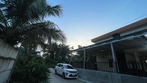 A white car parked on a dirt road beside a house with a metal roof and a gated fence. - Hotel O Pondok Ibu SyariahNearEco Edu Park (Pekanbaru)