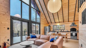 A modern log cabin interior with a large living area, kitchen, and large windows offering views of the outdoors.