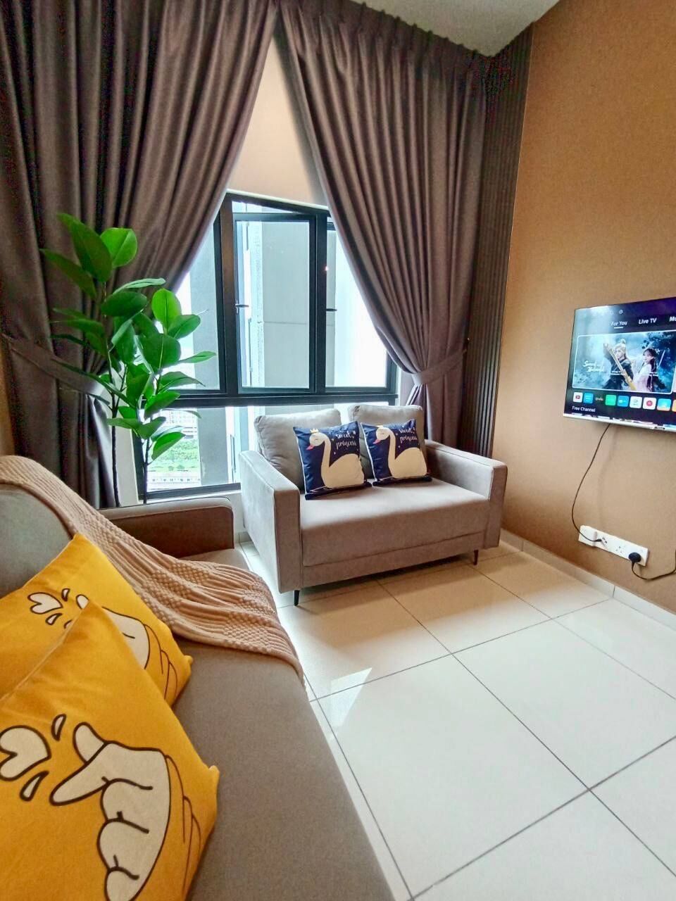 A living room with a sofa, a television, a window with curtains, and a plant.