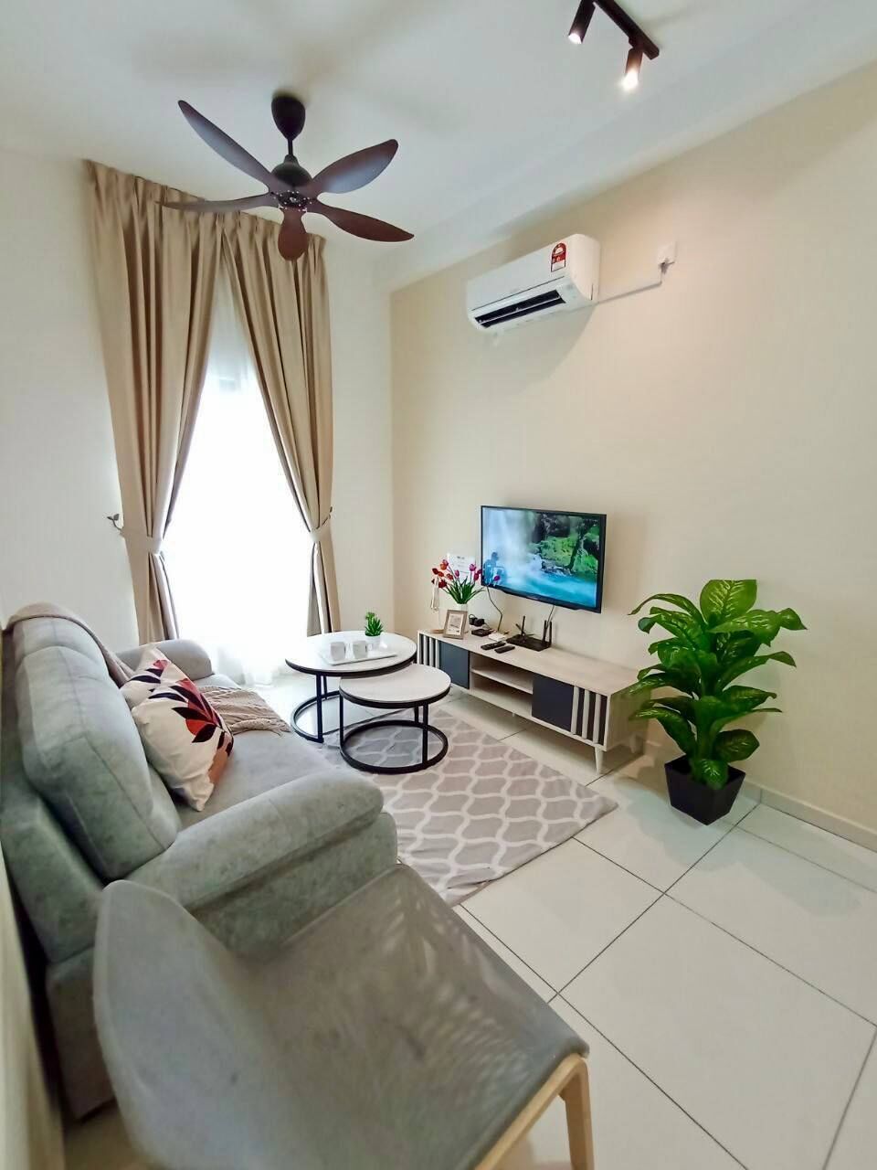A living room with a sofa, TV, ceiling fan, air conditioning unit, and a potted plant.