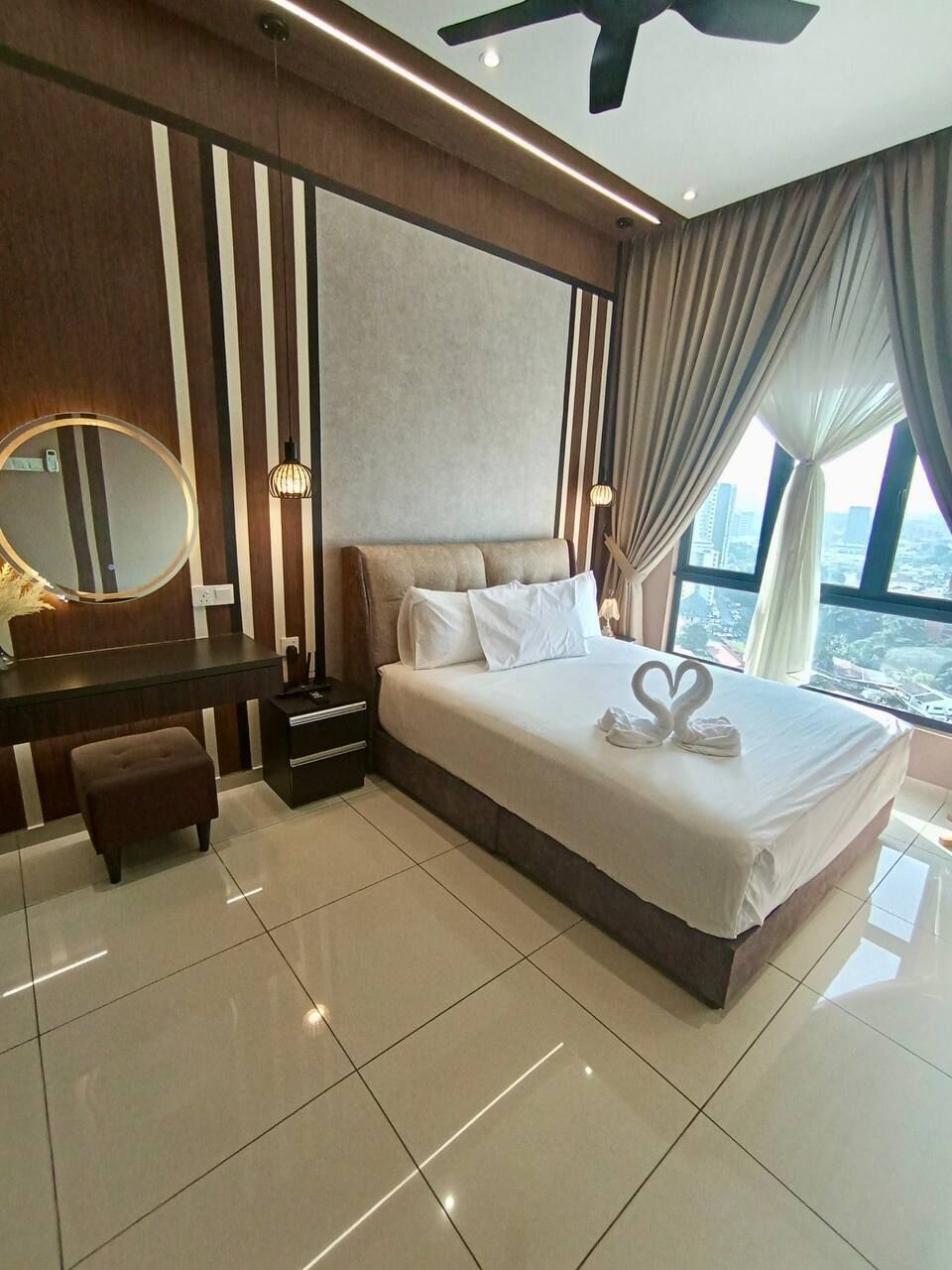 A hotel room with a large bed, a vanity with a mirror, a desk, and a view of the city.