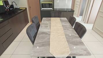 Un comedor moderno con una mesa de mármol, sillas tapizadas grises, un microondas integrado y una encimera de cocina.