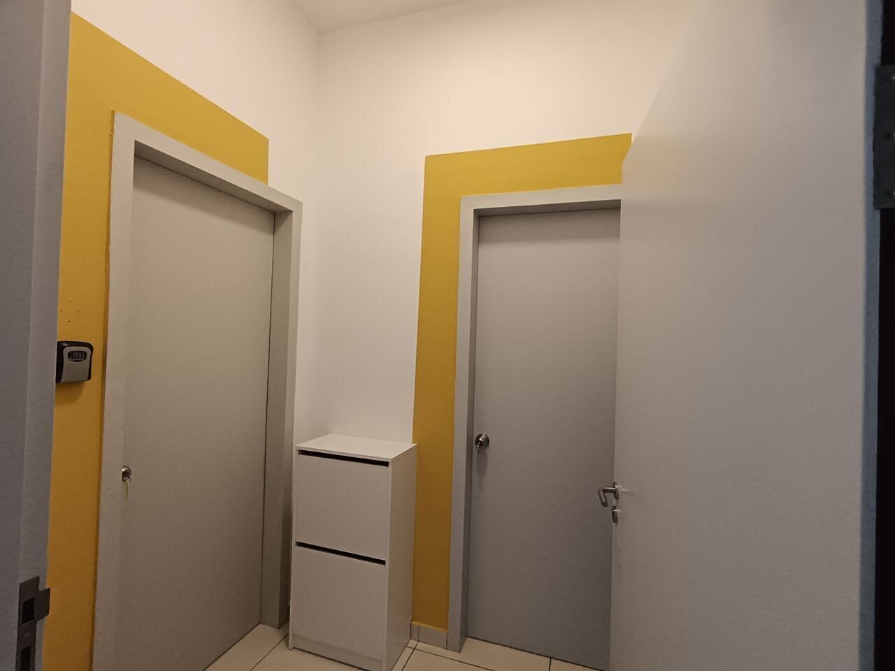A hallway with two doors, one with a yellow accent and a small white cabinet.