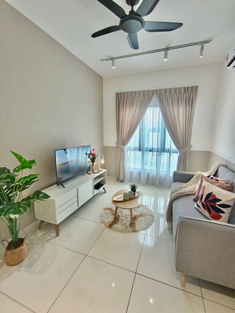 A modern living room with a flat-screen TV, a ceiling fan, a sofa, a coffee table, and a large window with curtains.