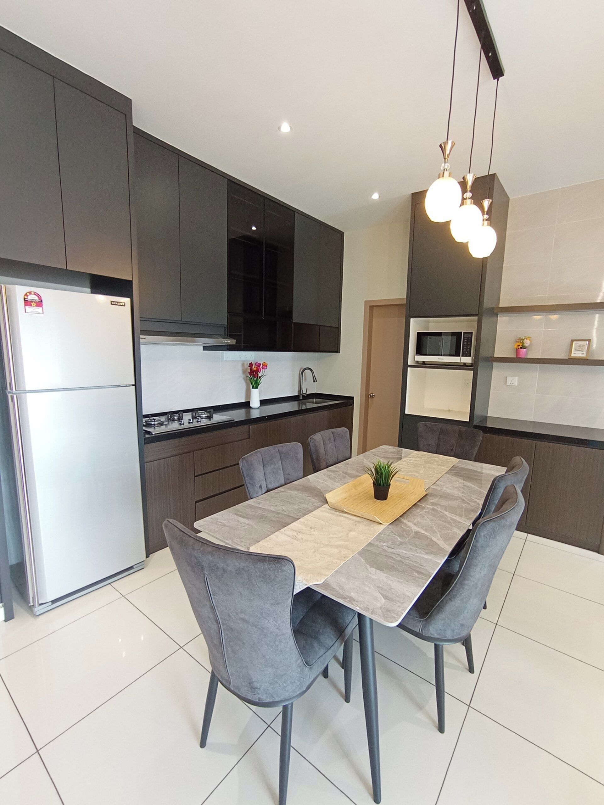 A modern kitchen with dark cabinets, a stainless steel refrigerator, a microwave, and a dining area with a table and chairs.