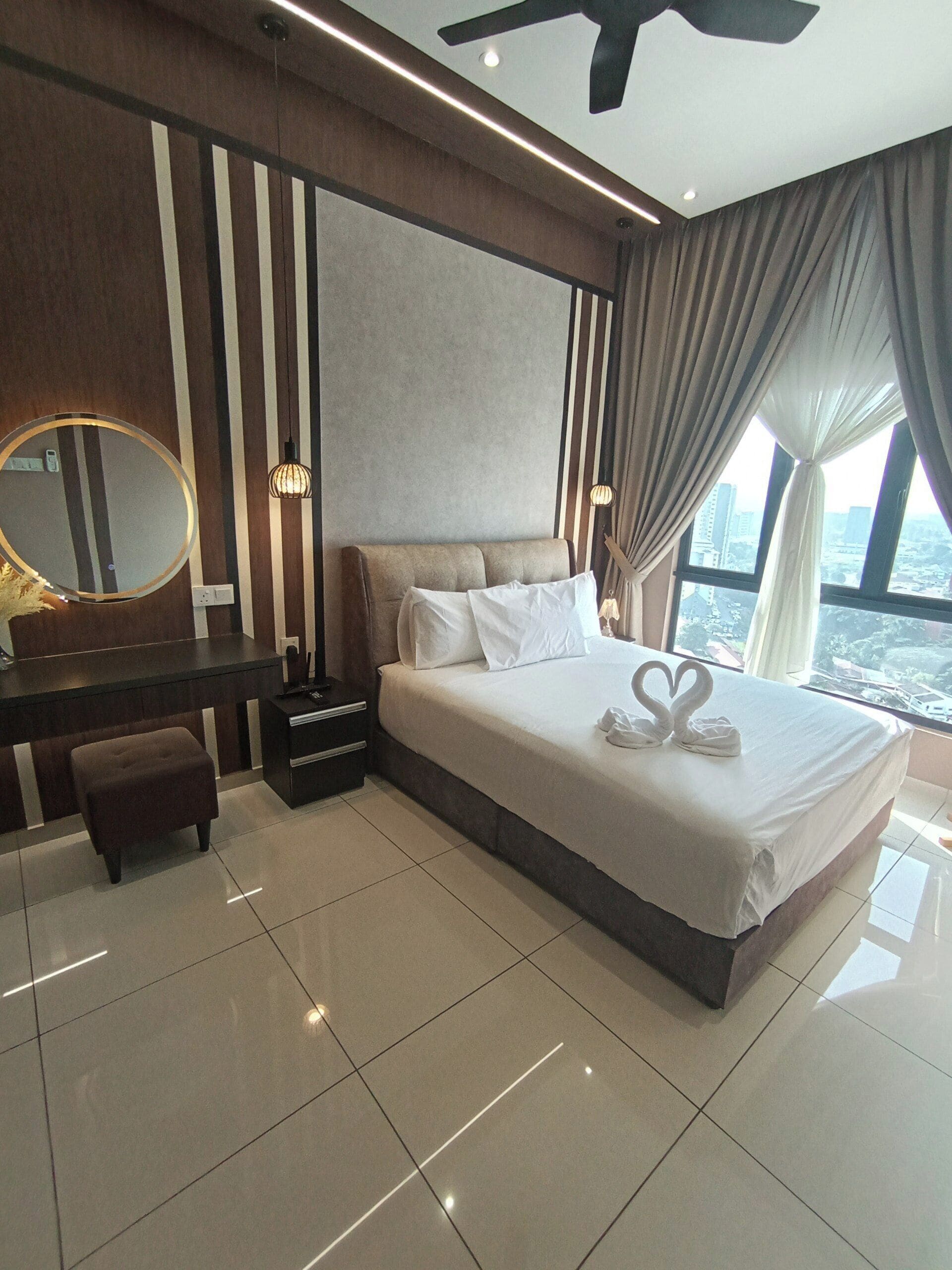 A modern hotel room with a large bed, a bedside table, a mirror, and a view of the city.