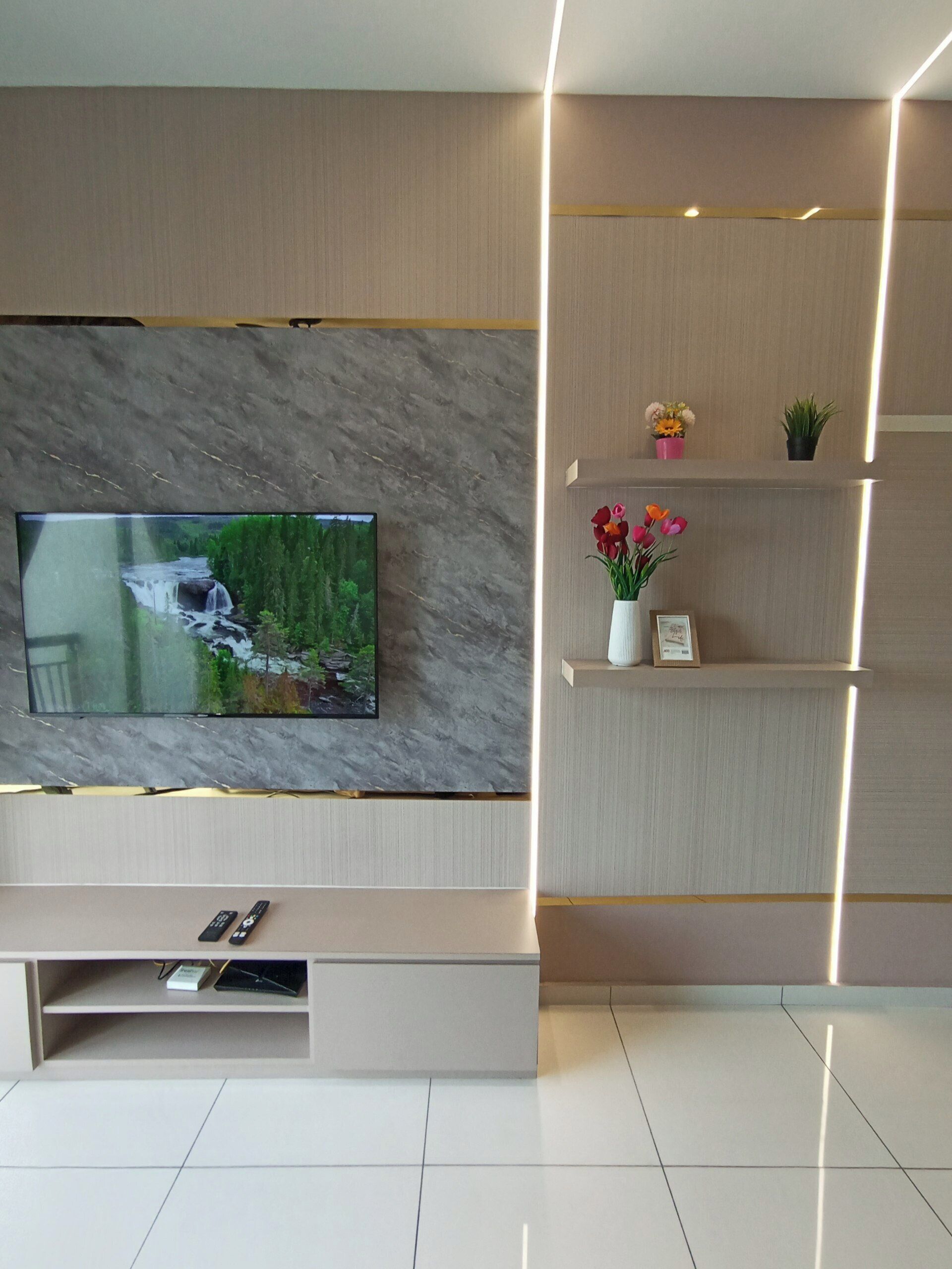 Un soggiorno moderno con una TV a schermo piatto montata su una parete strutturata, un mobile TV a incasso sottostante e uno scaffale decorativo con fiori.