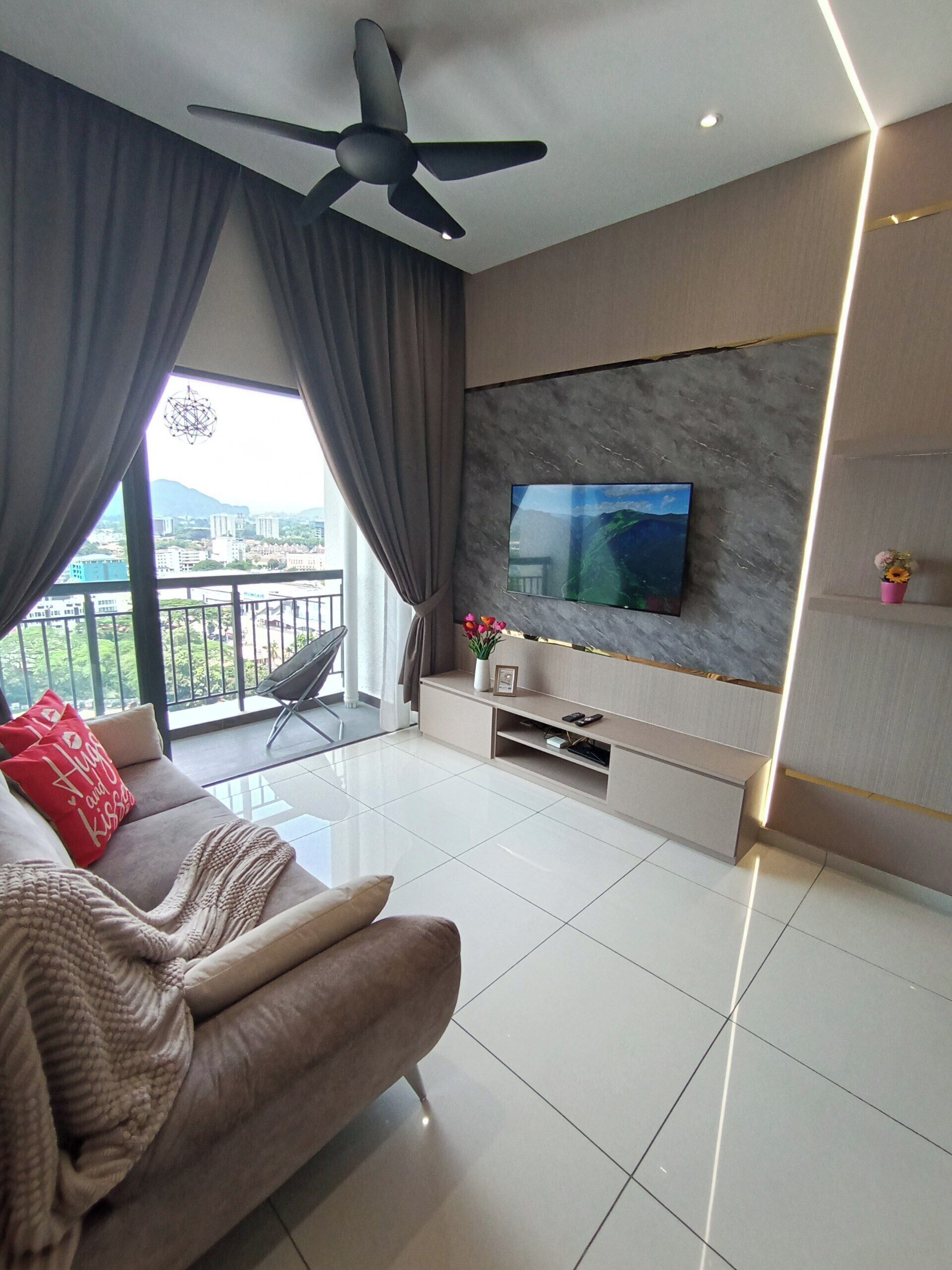 A modern living room with a sofa, a flat-screen TV mounted on a marble wall, a ceiling fan, and a balcony with a view of the city.