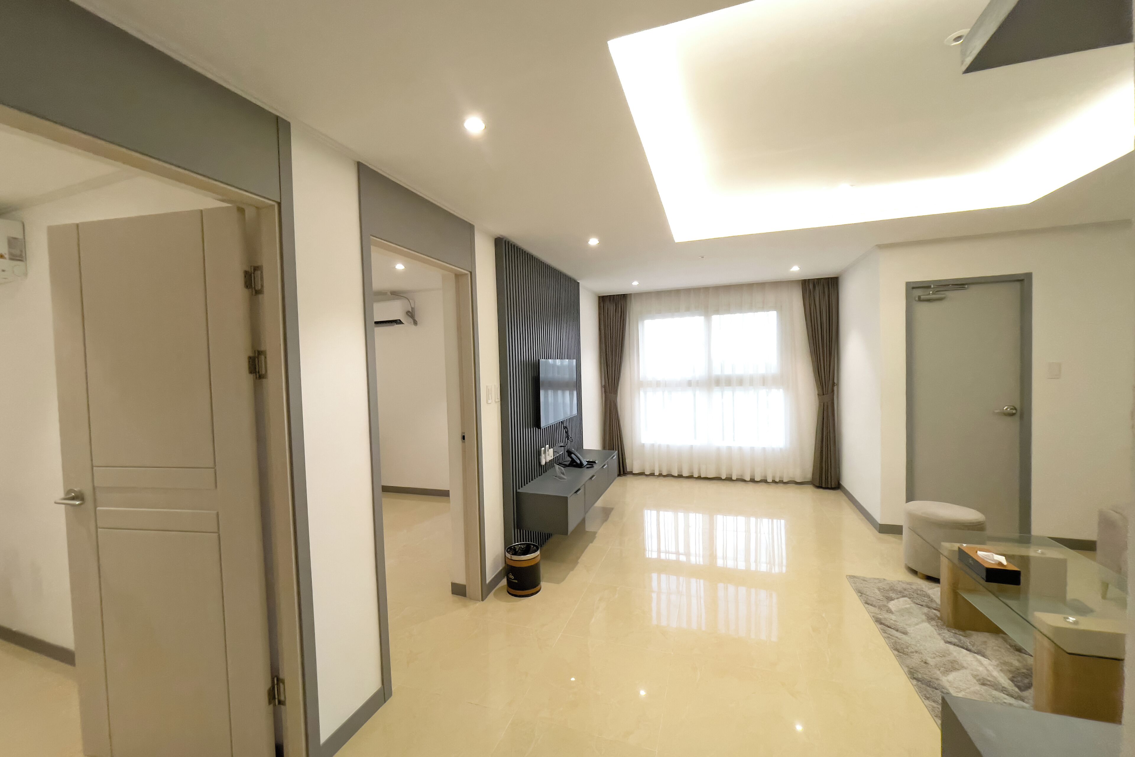 A modern hotel room with a large mirror, a flat-screen TV, a sofa, and a glass coffee table.