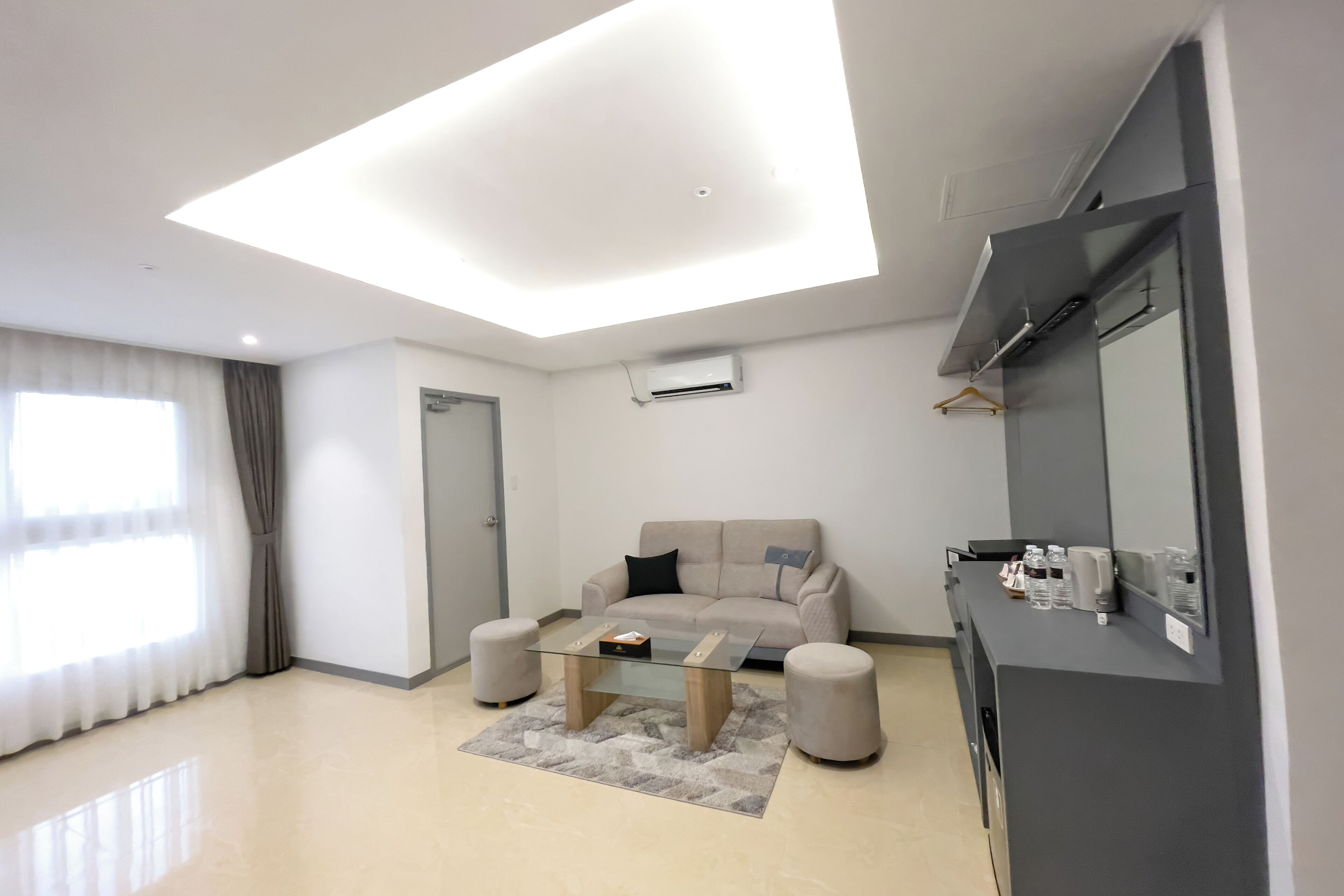Una sala de estar moderna con una mesa de centro de vidrio, un sofá color beige y dos otomanas.