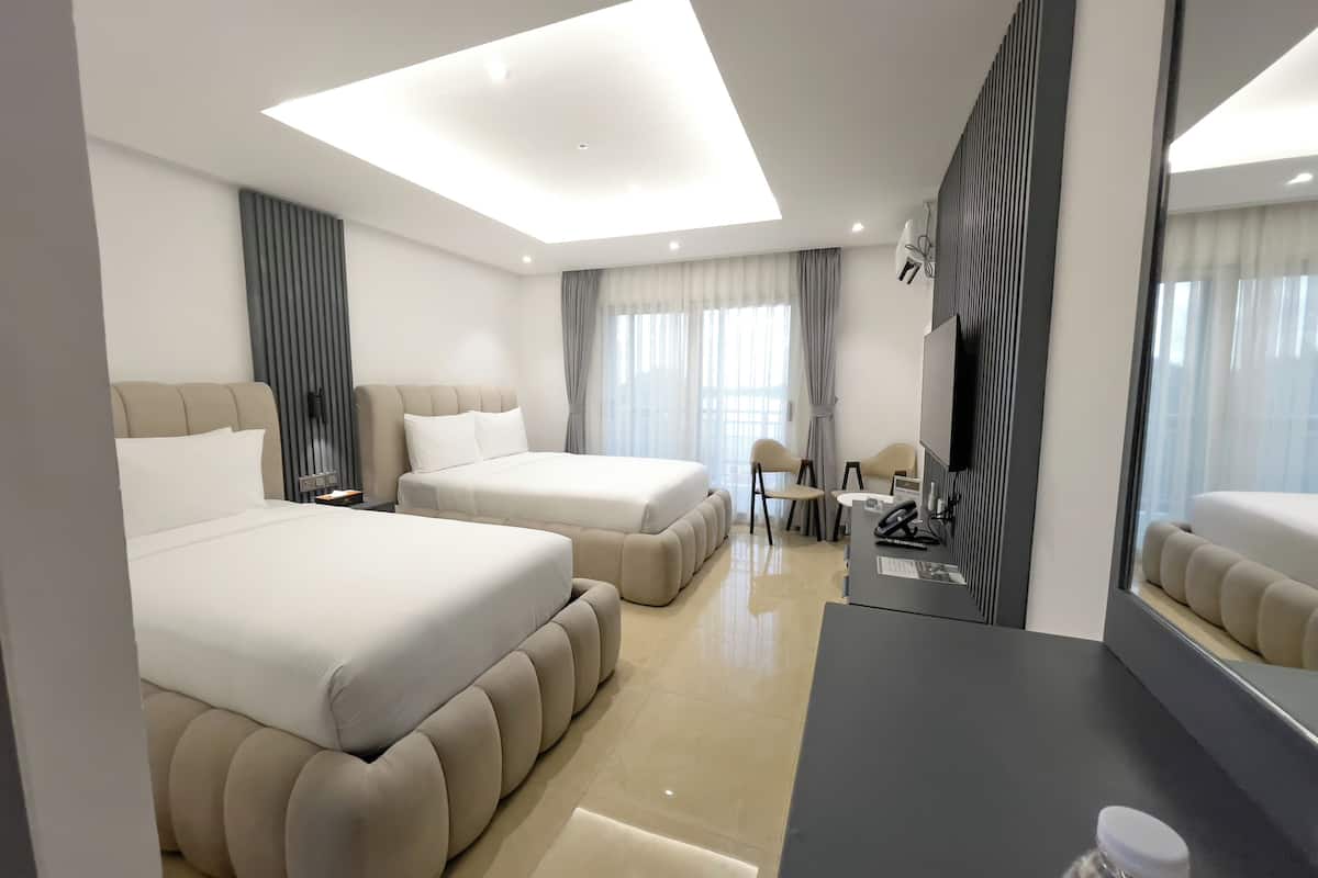 A modern hotel room with two large beds, a desk, and a chair.