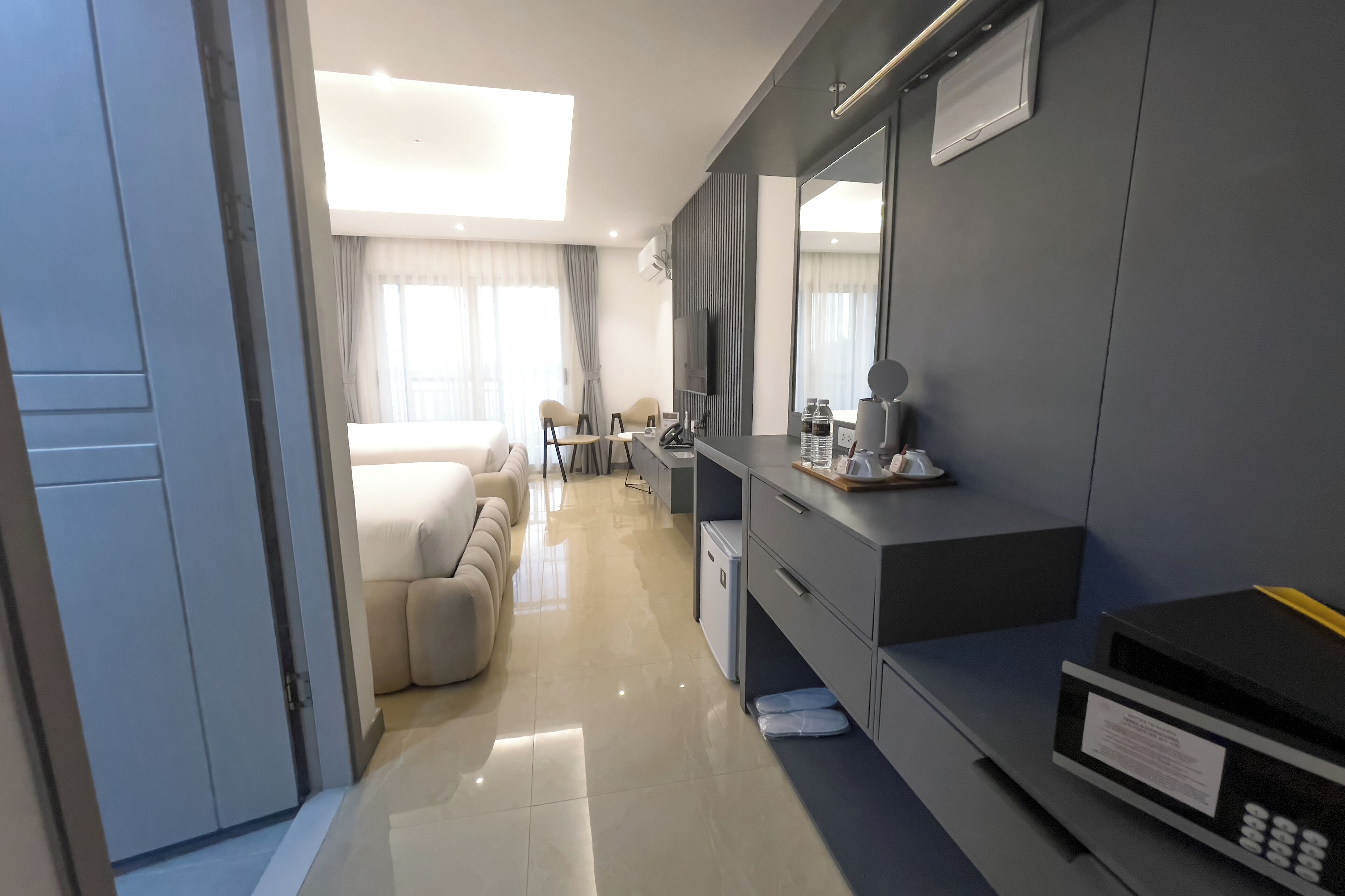 A modern hotel room with a large bed, a desk with a chair, a television, and a minibar.